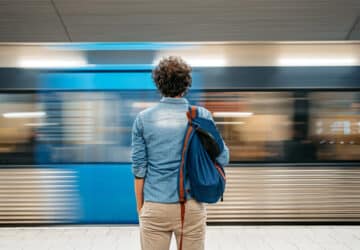 homem espera metro parar com a mochila virada para frente