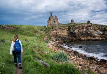 Mulher faz trilha próxima a castelo, com o seguro viagem Escócia