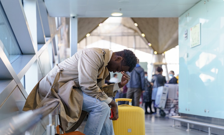 Rapaz sentado no aeroporto triste após cancelamento de viagem