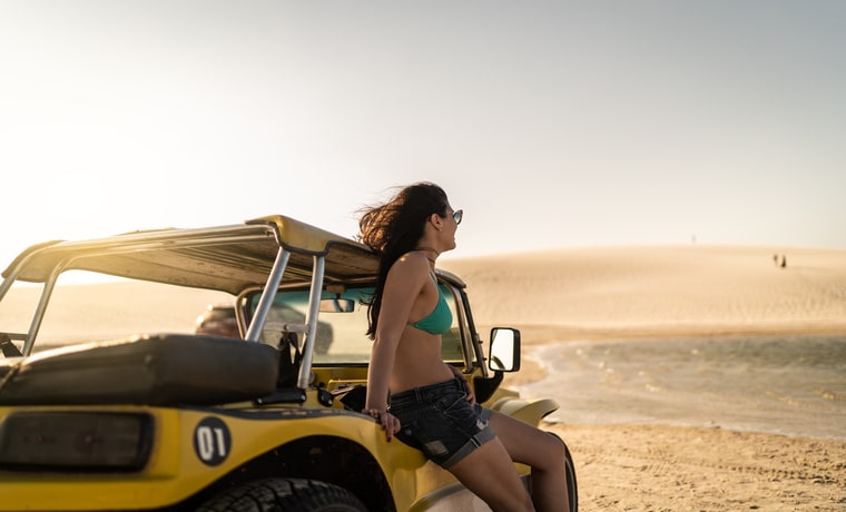 Mulher encostada em carro buggy admirando a paisagem das dunas da vila de Jericoacoara, no Ceará