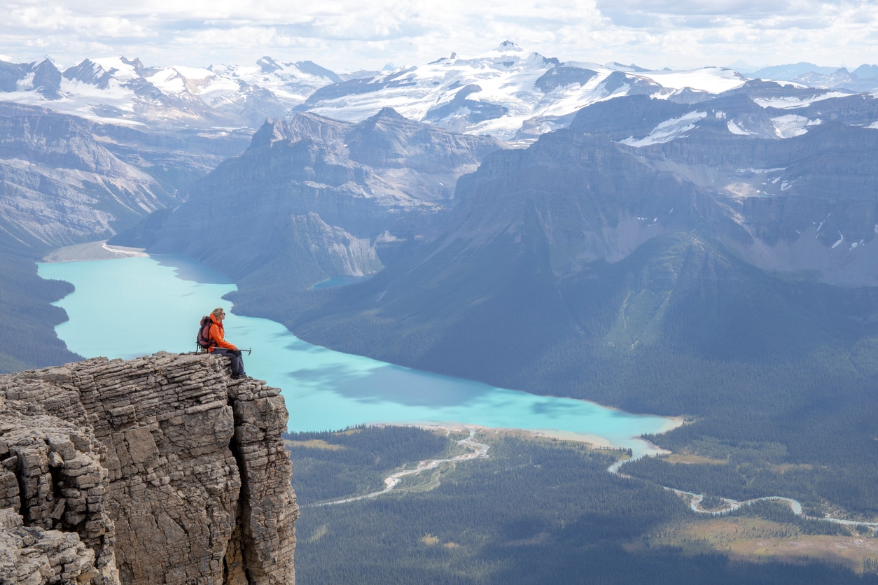 Homem sentado em um penhasco olhando a vista das montanhas rochosas canadenses e o lago Hector