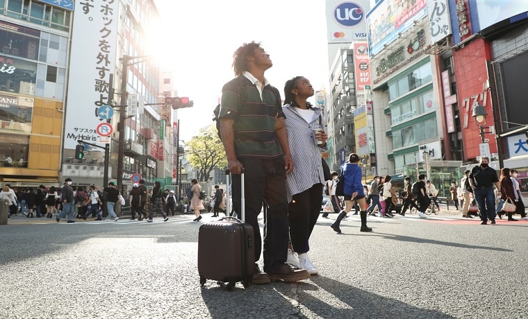 Homem e mulher em avenida japonesa, com mala de rodinha em mãos