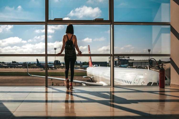 Mulher em pé na frente da janela do aeroporto, observando os aviões