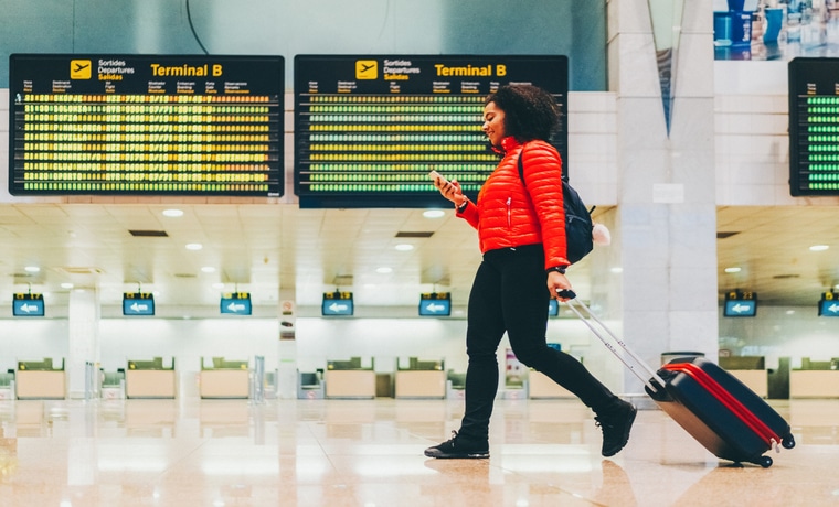 Mulher negra andando em um aeroporto, olhando seu celular