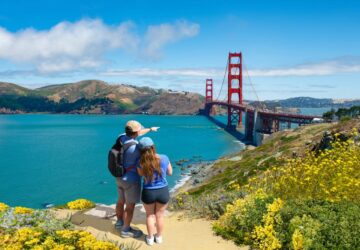 Casal de homem e mulher abraçados apontando para a Golden Gate, EUA