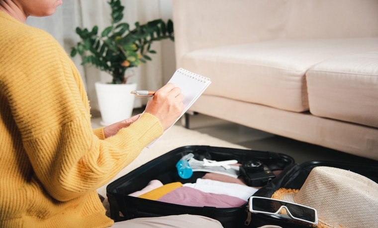 Mulher sentada no chão, fazendo a mala e conferindo o checklist de coisas para a viagem