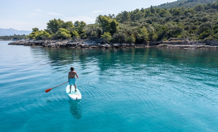 Homem em cima de pratica stand up paddle no mar da Croácia. 