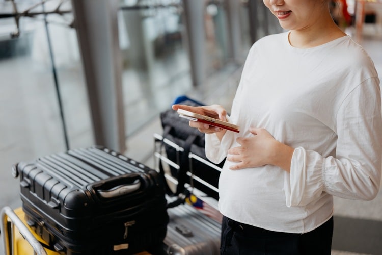 Mulher grávida no aeroporto lendo apólice do seguro viagem internacional para gestantes no celular.