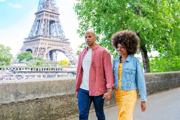 Viajantes que contrataram o seguro viagem Paris caminhando felizes pela cidade com a Torre Eiffel ao fundo. 