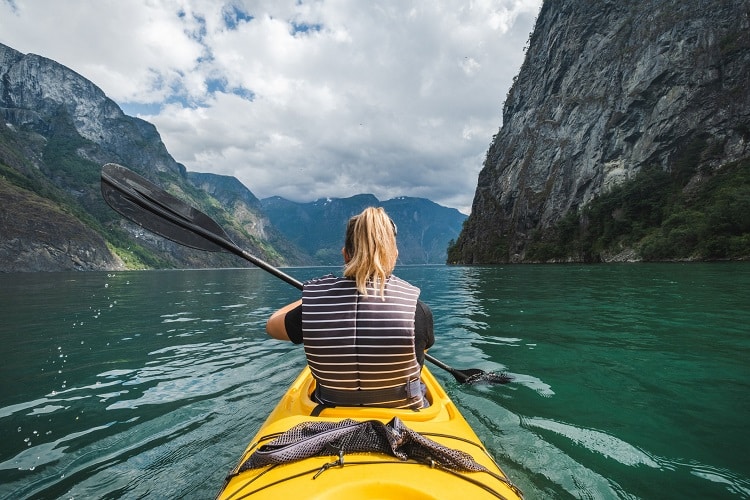 Mulher fazendo kayaking durante viagem. Para fazer esportes radicais na viagem, coberturas para traslados também são essenciais no seguro viagem.