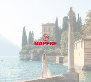 Mulher de vestido claro observando o lago e construções históricas na Itália. Em primeiro plano, logo da Mapfre