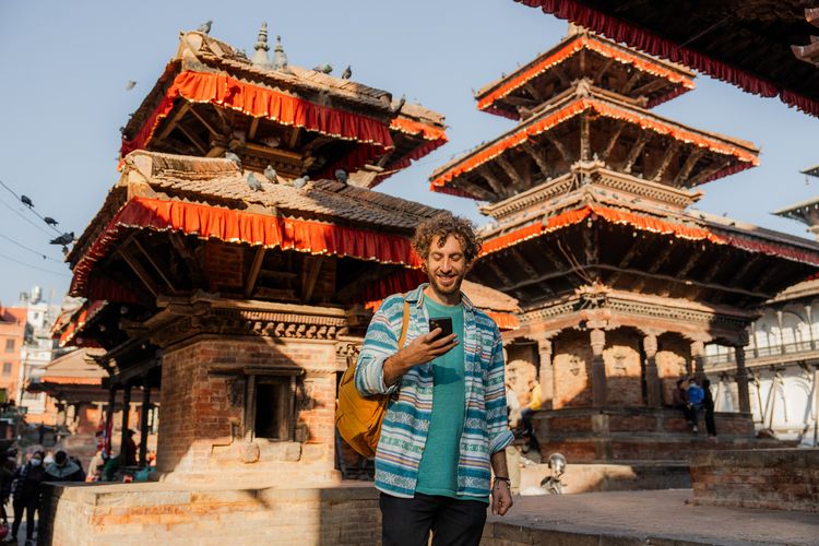 Homem acessando o Real Seguro Viagem pelo celular enquanto passeia por uma praça no Nepal. 