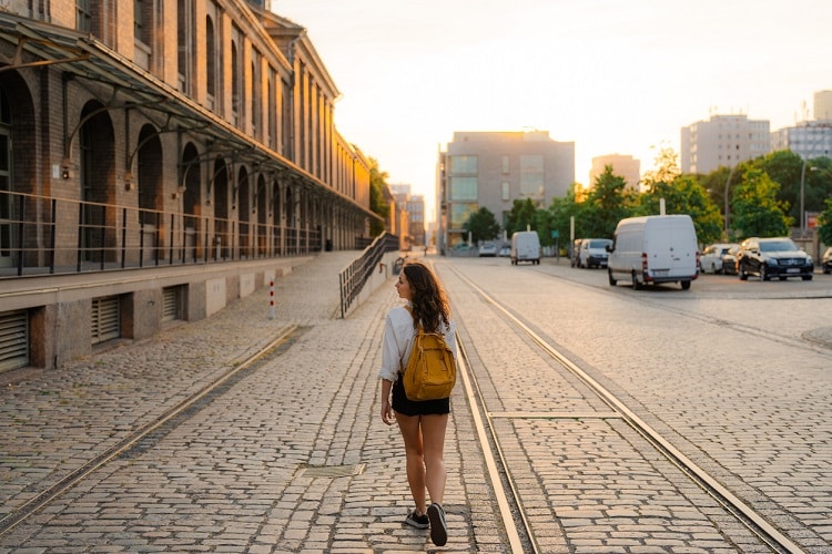 Menina andando por rua de Berlim, na Europa. Ela usa mochila de estudante.