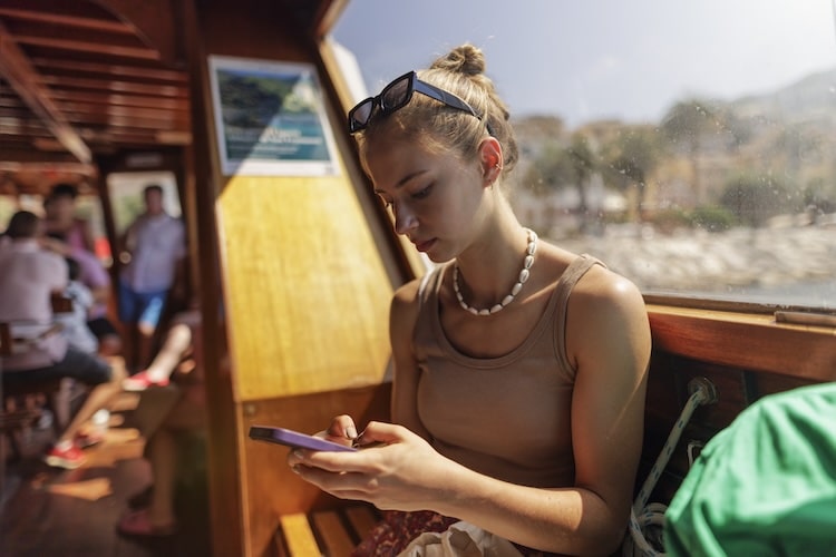 Turista adolescente viajando de barco usando smartphone.