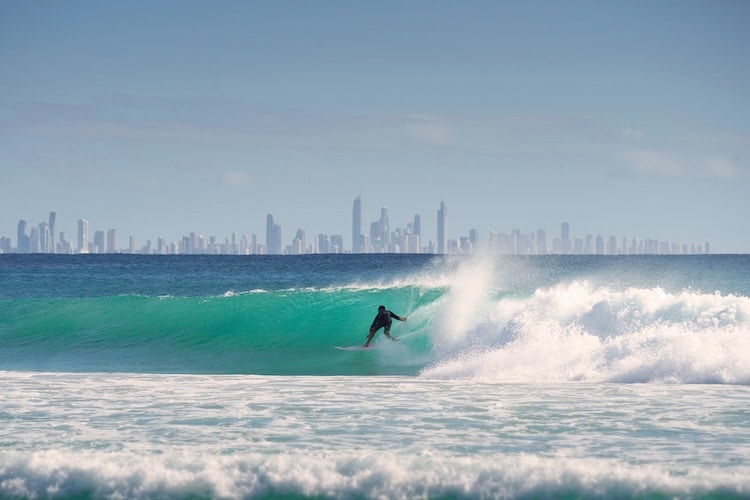 Surfista em uma onda no mar, ao fundo a cidade na Austrália.