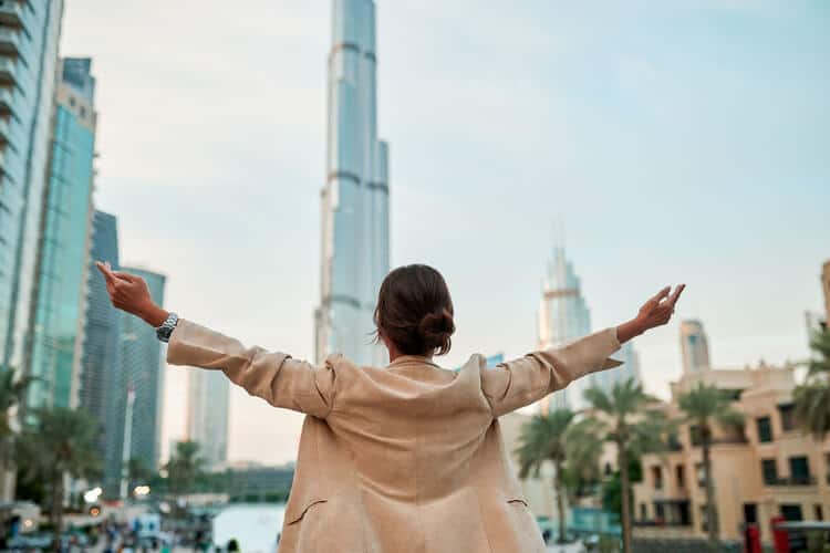 Pessoa com os braços abertos diante de arranha-céus modernos em Dubai.