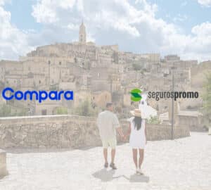 Casal caminhando de mãos dadas em uma cidade histórica de pedra sob um céu azul com nuvens. Em primeiro plano, logo da Compara Online ou Seguros Promo