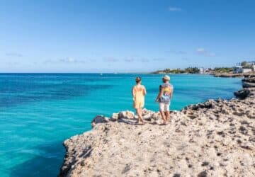 Casal caminhando sobre falésias à beira-mar em destino da América Central, com mar azul ao fundo.