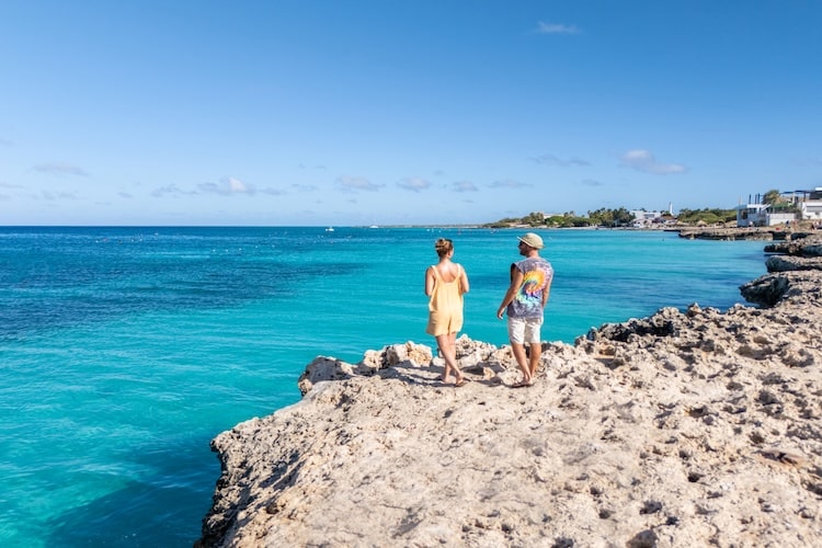 Casal caminhando sobre falésias à beira-mar em destino da América Central, com mar azul ao fundo.
